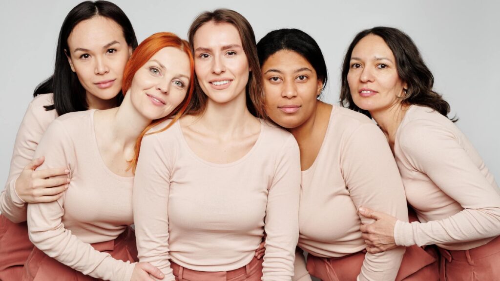 Five smiling women standing together, wearing coordinated outfits and expressing joy, confidence, and connection.